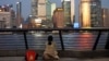 FILE - A woman sits on the bank of the Huangpu River in Shanghai and looks out at the Pudong financial district, Sept. 27, 2024.
