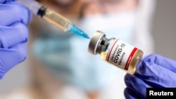 Seorang perempuan memegang botol kecil berlabel stiker "Coronavirus COVID-19 Vaccine" dan jarum suntik medis dalam ilustrasi ini diambil 30 Oktober 2020. (Foto: Reuters)