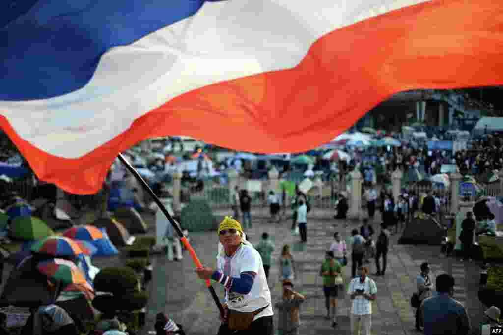A Thai anti-government protester waves a national flag during ongoing rallies at a protest site at Victory Monument in downtown Bangkok.&nbsp; A court threw the decision on whether to delay an election due to deadly unrest back to the government and election commission, leaving the controversial vote mired in uncertainty.
