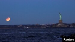 A "Super Blue Blood Moon" sets during a partial lunar eclipse next to the Statue of Liberty as it is seen from Brooklyn, in New York, Jan. 31, 2018. 
