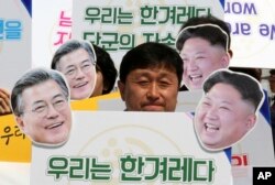 An activist with cutouts of South Korean President Moon Jae-in, left, and North Korean leader Kim Jong Un participates in a rally welcoming the planned summit between South and North Korea in Seoul, South Korea, April 25, 2018. The signs read: "We Are A Nation."