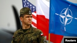 FILE - A Polish soldier stands in front of U.S., Polish and NATO flags ahead of military exercises in Swidwin, northwestern Poland.