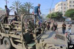 Warga Palestina mengendarai kendaraan militer Israel yang diambil dari pangkalan militer yang dikuasai militan Hamas di dekat pagar Jalur Gaza, di Kota Gaza, Sabtu, 7 Oktober 2023. (Foto: AP/Abed Abu Reash)