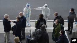 Seorang pekerja dengan penutup pelindung mengarahkan anggota tim Organisasi Kesehatan Dunia (WHO) pada saat kedatangan mereka di bandara di Wuhan di Provinsi Hubei China tengah pada hari Kamis, 14 Januari 2021. (Foto: AP)