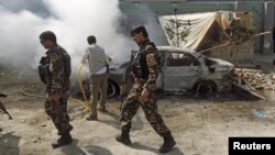 FILE - Afghan security forces walk past a burning car after a group of Taliban insurgents stormed a compound used by Afghanistan's intelligence agency in Kabul, Afghanistan, July 7, 2015.