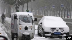 Seorang petugas pengantaran dengan motornya bergerak melewati mobil yang berselimut salju di di Beijing, China, pada 7 November 2021. (Foto: AP/Ng Han Guan)