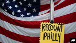 A sign hangs in front of an American flag, as a handful of supporters of President Donald Trump continue to protest outside the Pennsylvania Convention Center, in Philadelphia, Tuesday, Nov. 10, 2020. (AP Photo/Rebecca Blackwell)