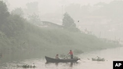 Warga mendayung perahu di Sungai Siak yang diselimuti kabut asap akibat kebakaran hutan di Pekanbaru, Riau (Oktober 2015). 