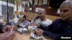 FILE - A currency exchange dealer counts U.S. currency at his shop in a shopping center in northern Tehran, Iran, Jan. 17, 2016. Iran's troubled currency fell to a new low against the U.S. dollar on Saturday.
