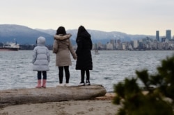 FILE - Maria Law, who emigrated from Hong Kong with her family, views the skyline with her daughters from Jericho Beach in Vancouver, British Columbia, Jan. 26, 2021.