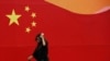 一名戴着口罩的女子在北京中部走过一面绘有中国国旗的墙壁。（资料照）
