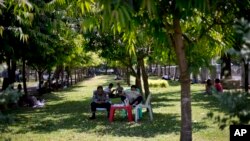 FILE - Police officers sit in the shade of a tree on a hot, humid day at a public park in Yangon, Myanmar, March 17, 2016.